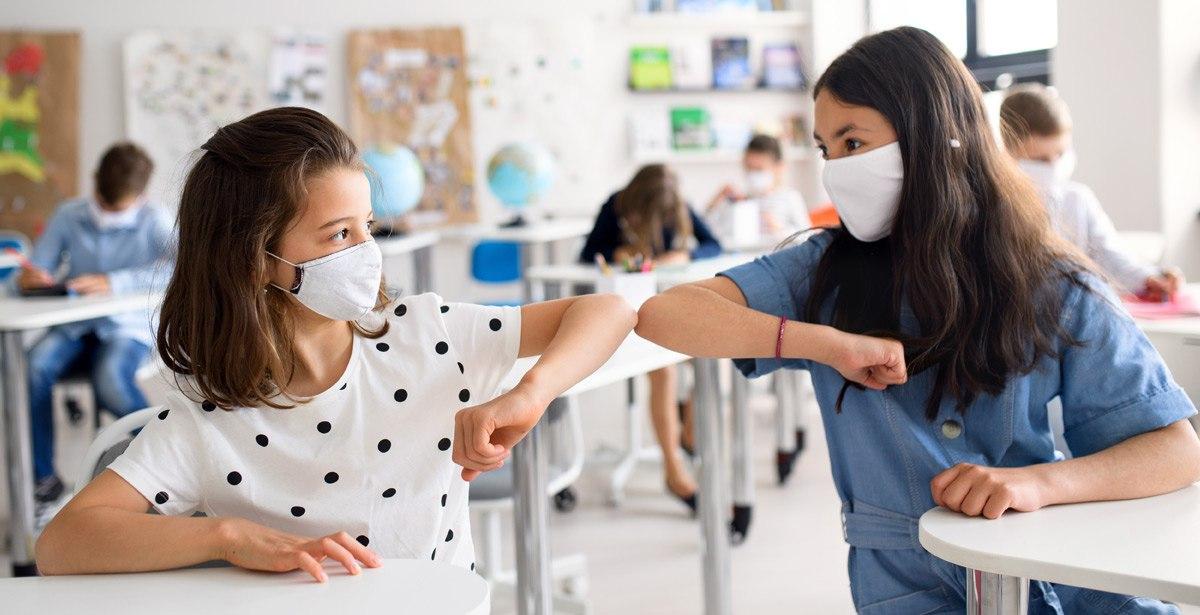 Bambine a scuola con mascherina e distanziamento - Foto di Halfpoint da Adobe Stock