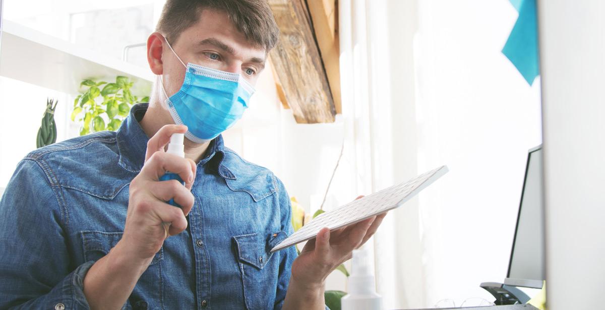 Giovane impiegato disinfetta la postazione di lavoro - Foto di karepa da Adobe Stock