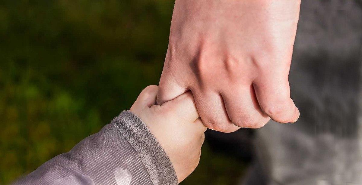 Testo alternativo: papà tiene la mano del figlio in abiti sdruciti
