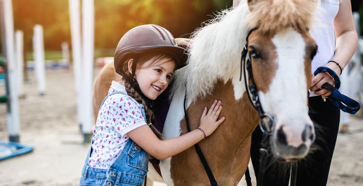 Bambina accarezza il suo pony al maneggio - Foto di hedgehog94 da Adobe Stock
