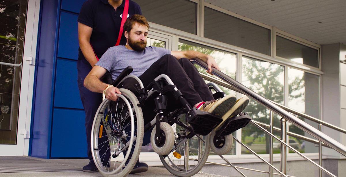 Assistente aiuta disabile in carrozzina a scendere le scale - Foto di Chudakov da Adobe Stock