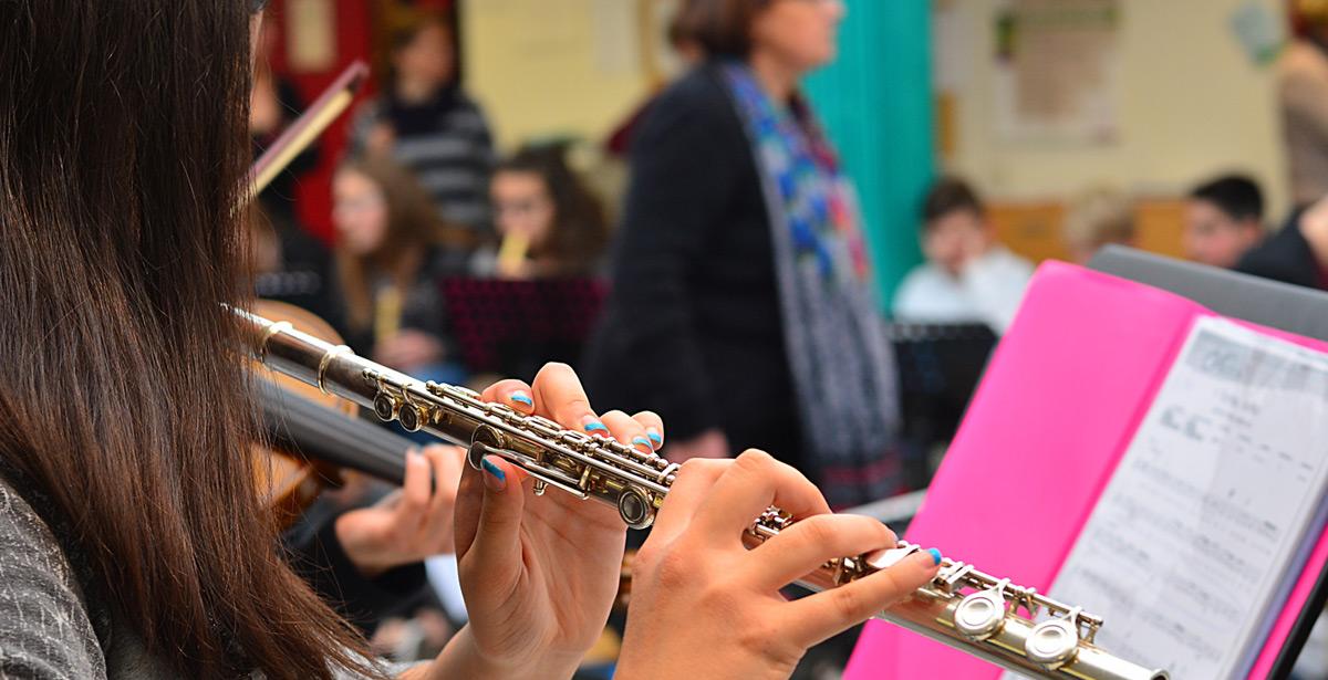 Ragazza suona il flauto traverso a scuola di musica con insegnante in background - Foto di liberowolf da Adobe Stock