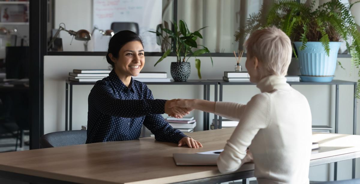 Due donne si stringono la mano sedute ad un tavolo - Foto di fizkes da Adobe Stock