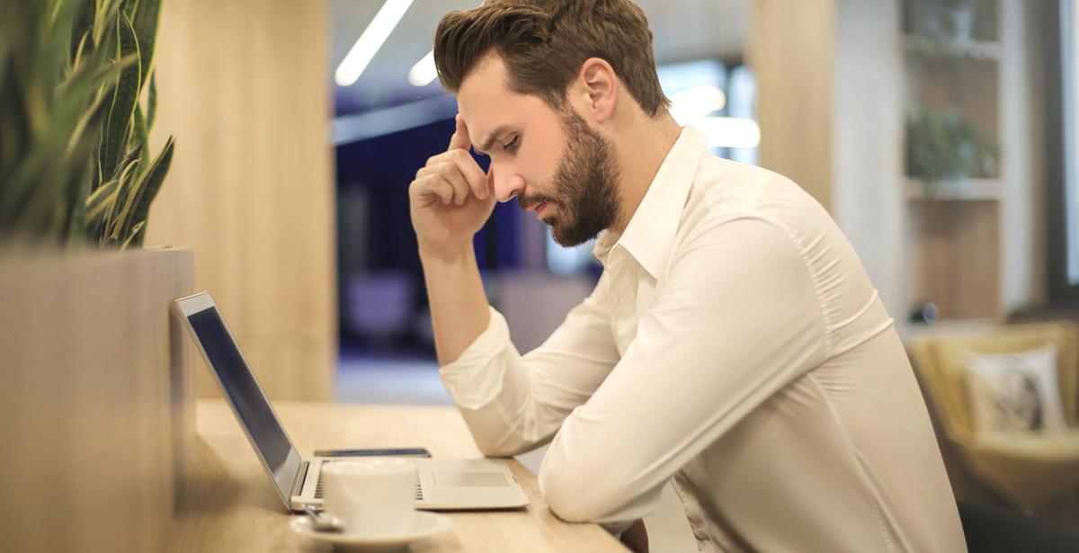 Uomo con la mano sulla tempio osserva il portatile - Foto di Andrea Piacquadio da Pexels.com