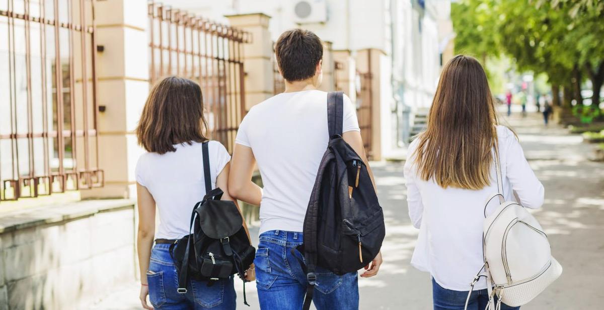 Due ragazze ed un ragazzo, di spalle, con gli zaini, camminano in strada